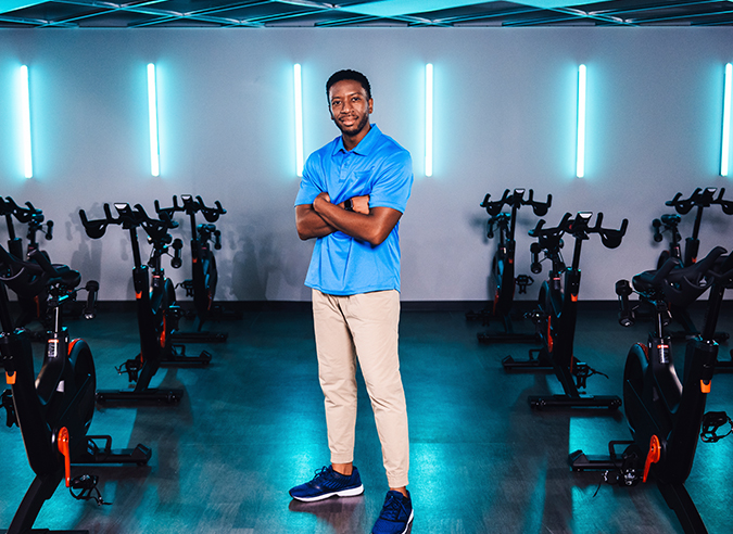 A man with crossed arms standing in a spinning class studio